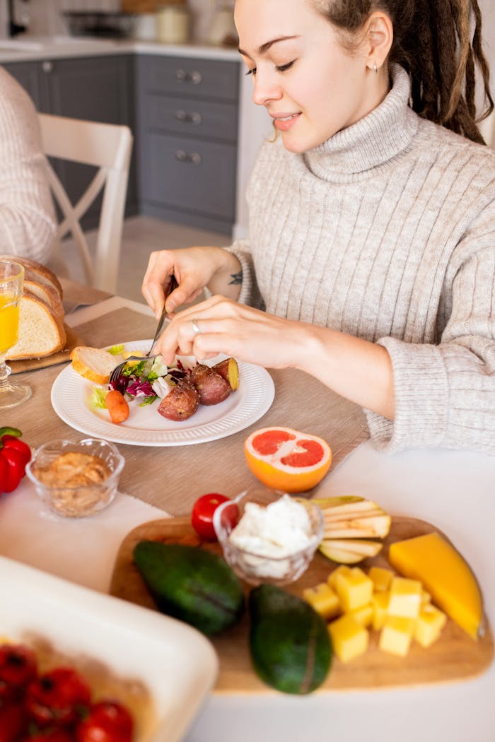 A woman in a cozy sweater enjoys a healthy breakfast with fruit and salad indoors.